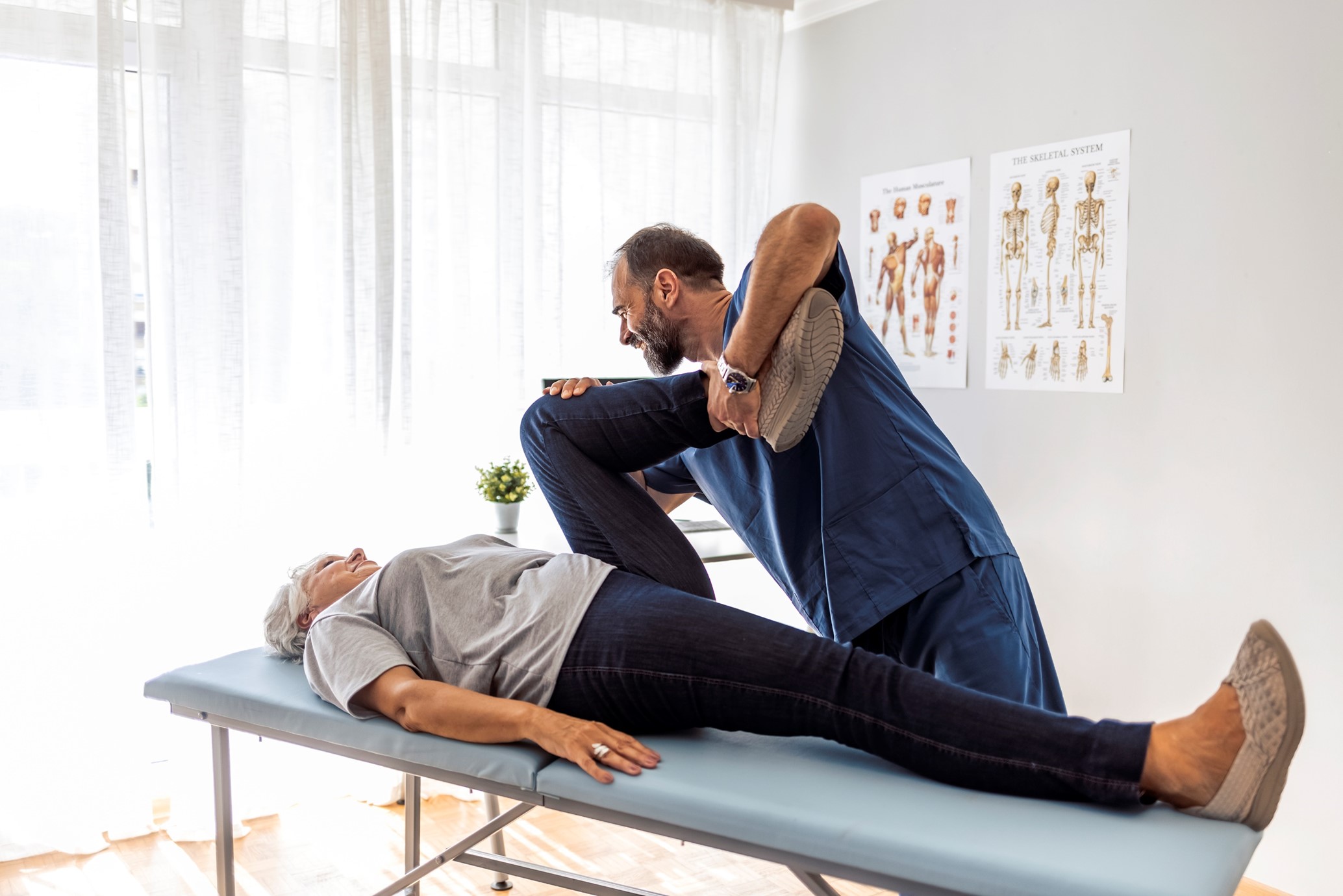 a person lying on a bed and a physoptherapsit bending their leg