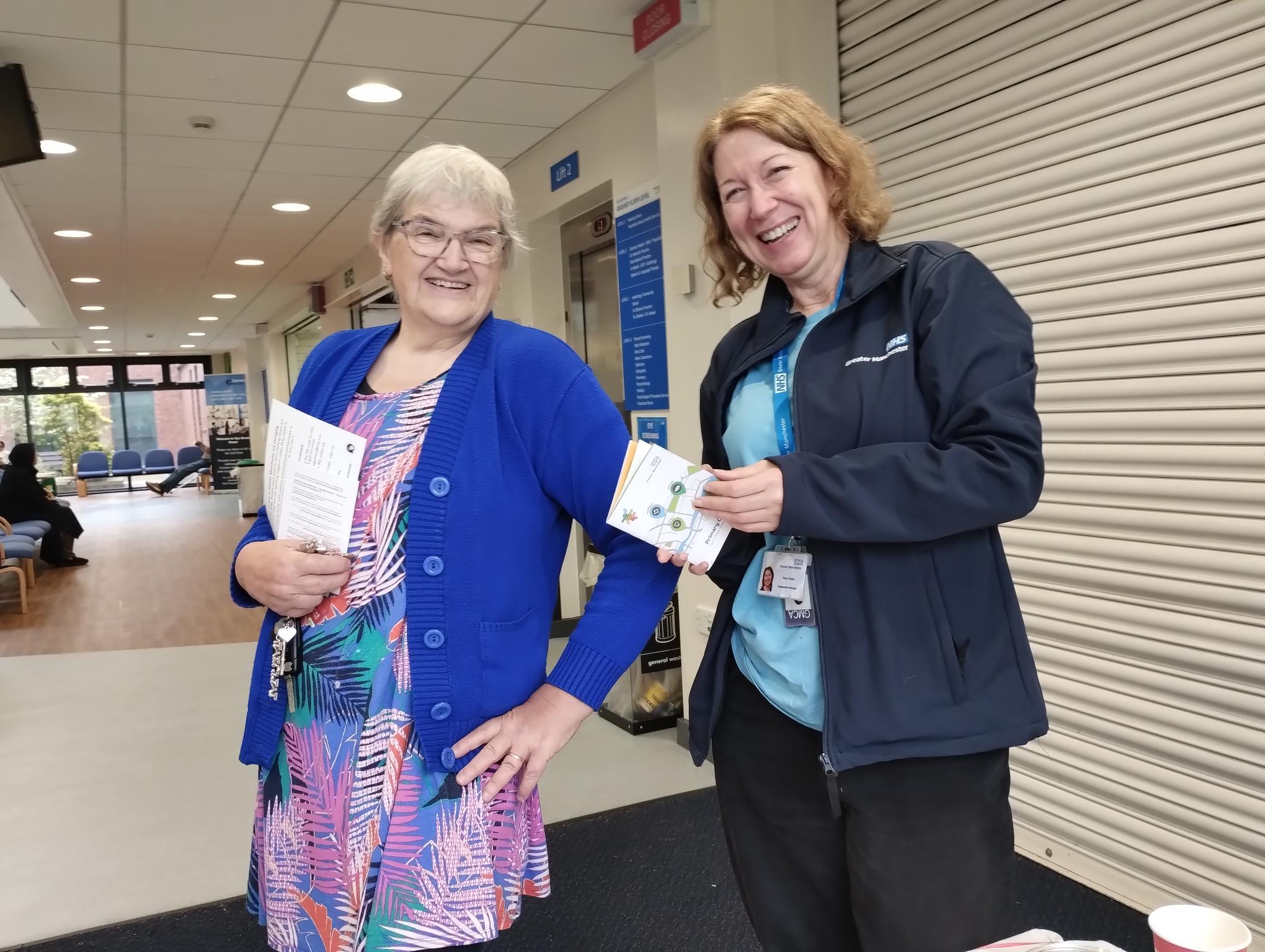 A member of the engagement team with a smiling member of the public holding the information and leaflets in a health setting