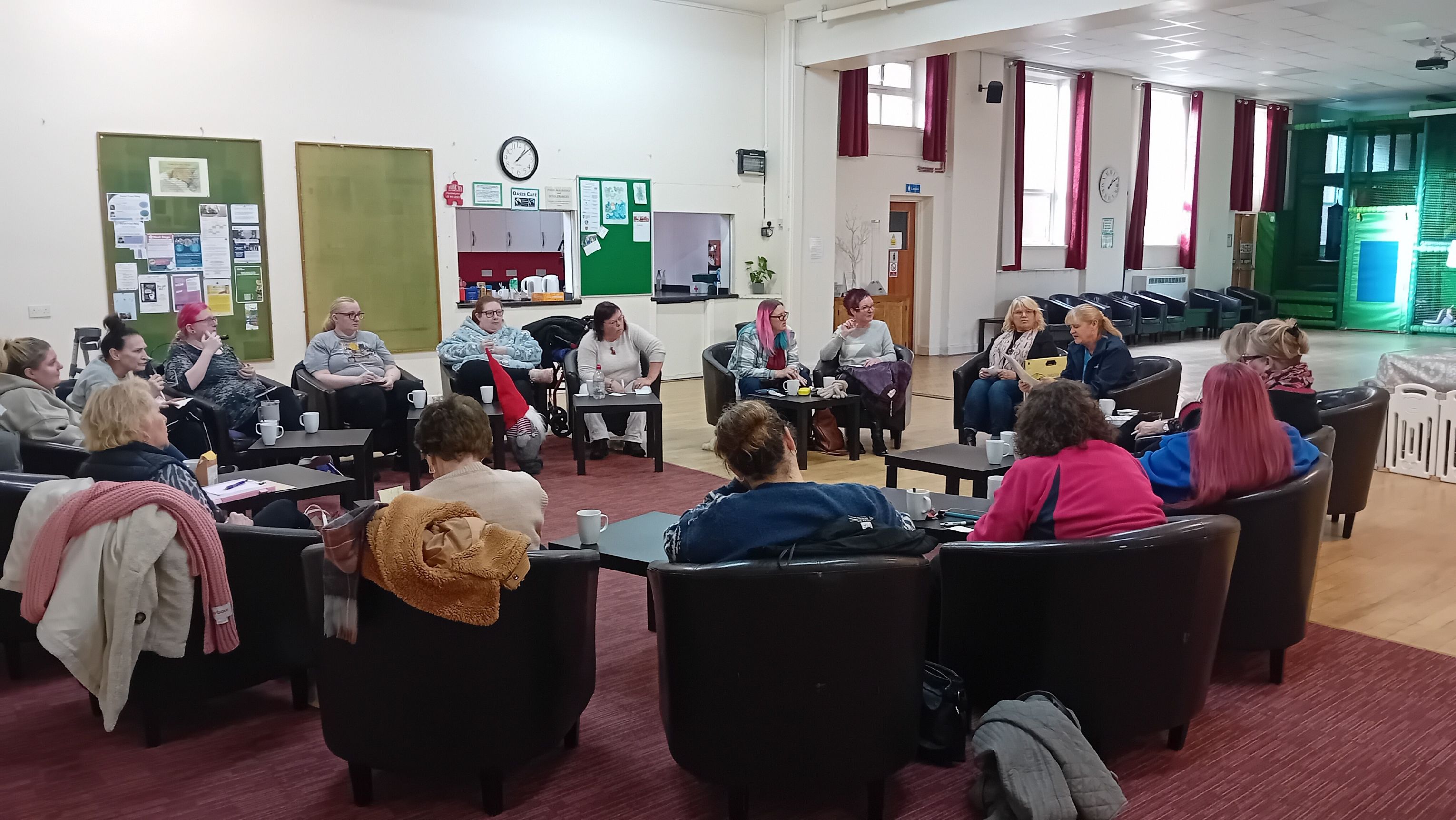 A ladies group sitting in a circle talking to a member of the NHS GM engagement team at a community venue