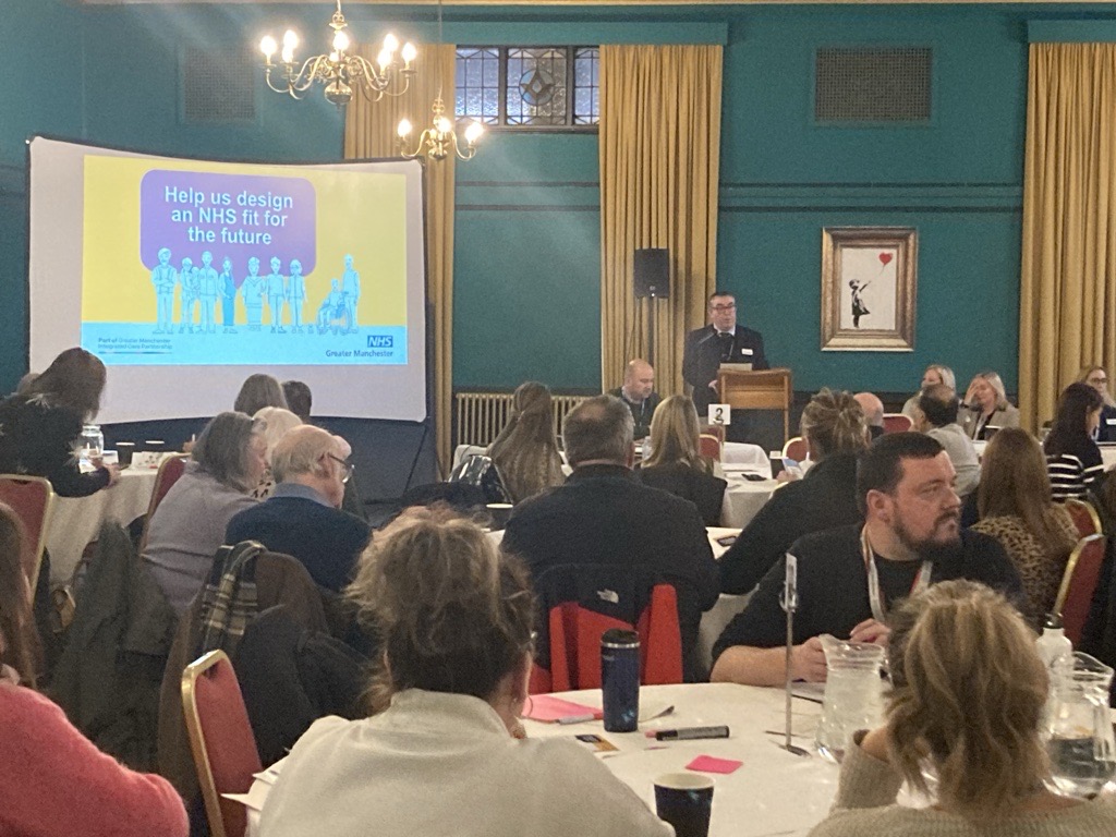 A photo of an NHS GM event in Stockport with a presenter in front of a room